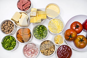 Top view of pizza ingredients separated in bowls - tomatoes, cheese, pineapple chunks, pepperoni, mushrooms, bacon, bell peppers