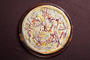 Top view of a pizza on a wooden cutting board with a brown background