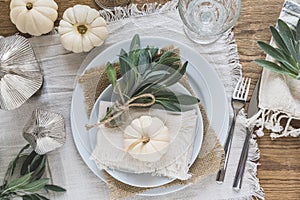 Top view of place setting on a wooden table with white mini pumpkins, sage leaves and crystal glasses for Thanksgiving Day or