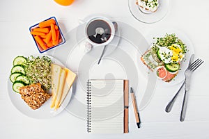 Top view planning notebook with copy space and healthy breakfast. Sandwich with egg benedict and smoked salmon, plate with cheese,