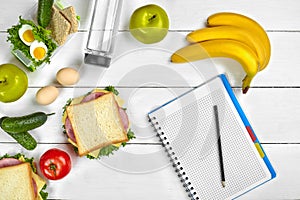 Top view planning notebook with copy space and healthy breakfast. Sandwich with ham and cheese, eggs, cucumber, tomato