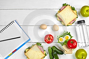 Top view planning notebook with copy space and healthy breakfast. Sandwich with ham and cheese, eggs, cucumber, tomato