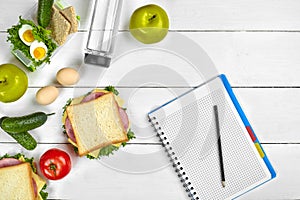 Top view planning notebook with copy space and healthy breakfast. Sandwich with ham and cheese, eggs, cucumber, tomato