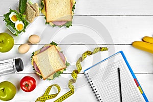 Top view planning notebook with copy space and healthy breakfast. Sandwich with ham and cheese, eggs, cucumber, tomato