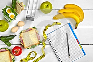 Top view planning notebook with copy space and healthy breakfast. Sandwich with ham and cheese, eggs, cucumber, tomato