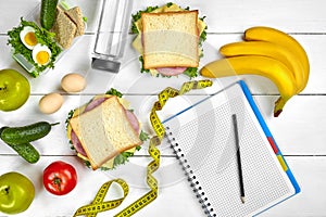 Top view planning notebook with copy space and healthy breakfast. Sandwich with ham and cheese, eggs, cucumber, tomato