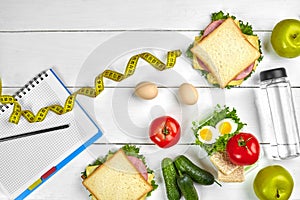 Top view planning notebook with copy space and healthy breakfast. Sandwich with ham and cheese, eggs, cucumber, tomato