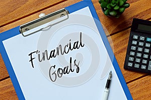 Top view of plant,calculator,pen and clipboard written with Financial Goals on wooden background.