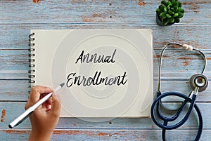 Top view of plant,stethoscope, and hand writing Annual Enrollment on notebook on wooden background photo