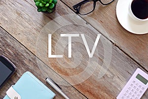 Top view of plant, sunglasses, a cup of coffee, calculator, pen, notebook,and mobile phone on wooden background written with LTV.