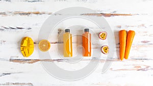 Top view of a plastic bottles of fruit and vegetable juice with apple carrot orange and mango place around on a rustic wooden