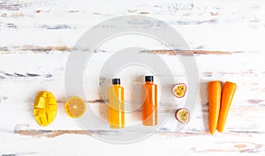 Top view of a plastic bottles of fruit and vegetable juice with apple carrot orange and mango place around on a rustic wooden