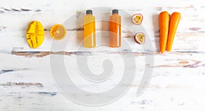 Top view of a plastic bottles of fruit and vegetable juice with apple carrot orange and mango place around on a rustic wooden