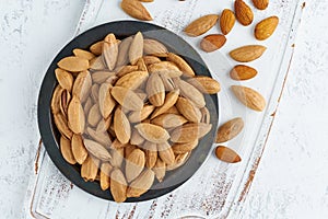 Top view plate with almonds in endocarp, bowl with drupe in shell on a white wooden cutting board. White background, overhead,