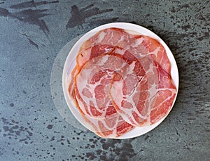 Top view of a plate of dry coppa on a gray mottled tabletop photo