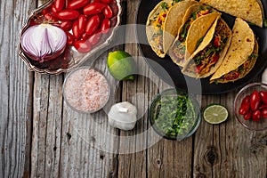 Top view of plate with hot mexican tacos on rustic wooden table with ingredients for cooking background. Concept of traditional