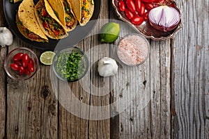 Top view of plate with mexican tacos on rustic wooden table with ingredients for cooking background. Concept of traditional meal.