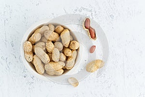 Top view plate with peanut in endocarp, bowl with drupe in shell on a white table. Stone background, overhead, copy space, close photo