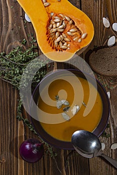 Top view on a plate with pumpkin soup on a wooden table with vegetables, thyme and seeds