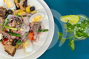 Top view of a plate of Salade nicoise and glass of mojito on blue table