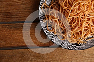 Top view of a plate with tomato spaghetti on a wooden table