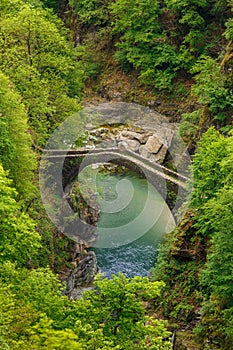 Top view on the Ponte Romano Intragna Bridge hiding in the valley with beautiful river covered with trees, close to