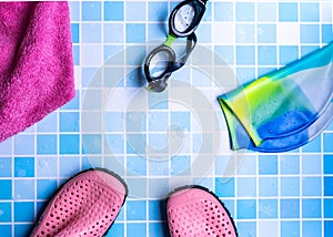 Top view of pool shoes, goggles, cap, and a towel on blue-tiled surface for a copy space