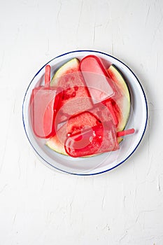 Top view of popsicles on plate with watermelon pieces, white background