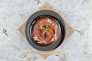 Top view of Pork rib chops steaks boiled with tomato sauce and cheese served in black round plate with chopstick on makisu.