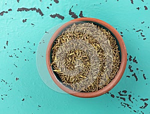 Top view of a portion of organic thyme leaf in a small bowl atop a green and black mottled countertop