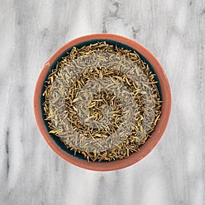 Top view of a portion of organic thyme leaf on a small bowl atop a marble countertop