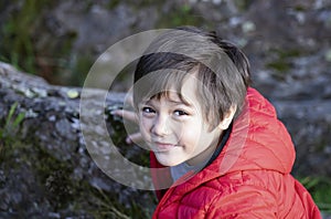 Top view portrait of cute little boy standing next to stone rocks and looking up camera with smiling face, Active child Playing