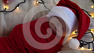 Top View Portrait First Days Of Life Newborn Cute Funny Sleeping Baby In Santa Hat Wrapped In Red Diaper At White