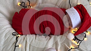 Top View Portrait First Days Of Life Newborn Cute Funny Sleeping Baby In Santa Hat Wrapped In Red Diaper At White