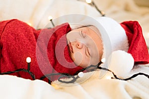 Top View Portrait First Days Of Life Newborn Cute Funny Sleeping Child Baby In Santa Hat Wrapped In Red Diaper At White