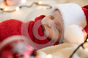 Top View Portrait First Days Of Life Newborn Cute Funny Sleeping Child Baby In Santa Hat Wrapped In Red Diaper At White