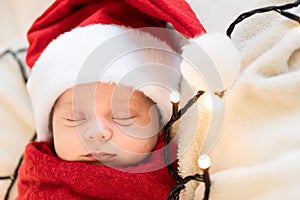 Top View Portrait First Days Of Life Newborn Cute Funny Sleeping Child Baby In Santa Hat Wrapped In Red Diaper At White