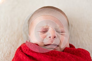 Top View Portrait First Days Of Life Newborn Funny Sleeping crying face close Baby child Wrapped In Red Diaper At White