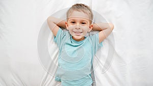 Top view portrait of happy smiling toddler boy lying on bed and laughing in the camera. Concept of happy children having