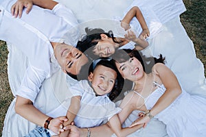 Top view portrait of a joyous asian family in white clothes lying on a blanket