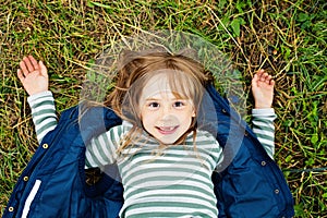 Top view portrait of a pretty child girl in blue jacket relaxing on a grass