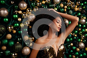 Top view portrait of stunning lady posing lying on emerald silky texture decorated with xmas tree glitter baubles