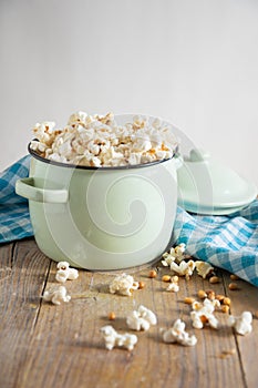 Top view of pot with fresh popcorn on rustic wooden table with blue cloth, white background