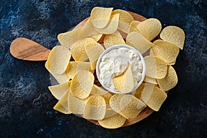 Top view potato chips, sauce in a white bowl on a wooden cutting board