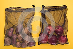 Top view of potatoes and apples in eco friendly black mesh bags isolated on yellow.