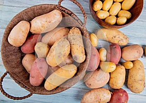 top view of potatoes in basket with new ones in bowl and others of different types on wooden background