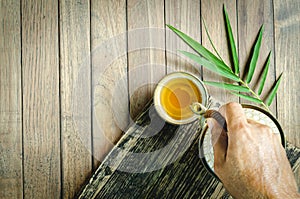 Top view pouring hot tea from a teapot into cupping,  bamboo leaves on the old wood table.