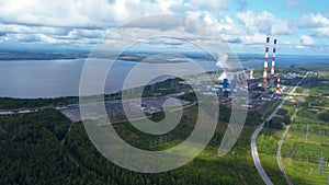 Top view of power plant on lake shore. Clip. Factory pipes on background of lake and green forest. Landscape with power