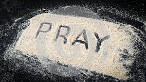Top view of PRAY text written on white sand