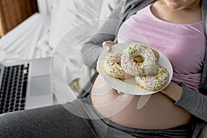 Top view of pregnant woman with few donuts on plate